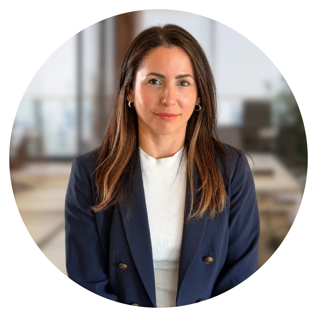 Professional headshot of a woman with long brown hair wearing a navy blazer and white top seated in an office setting
